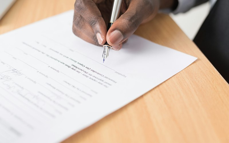 A hand signing a formal legal document with a fountain pen