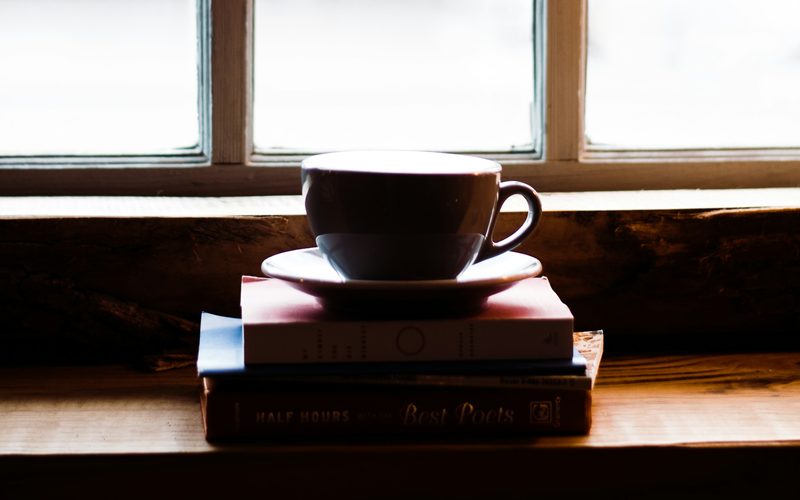 A cup and saucer on a stack of books by a window