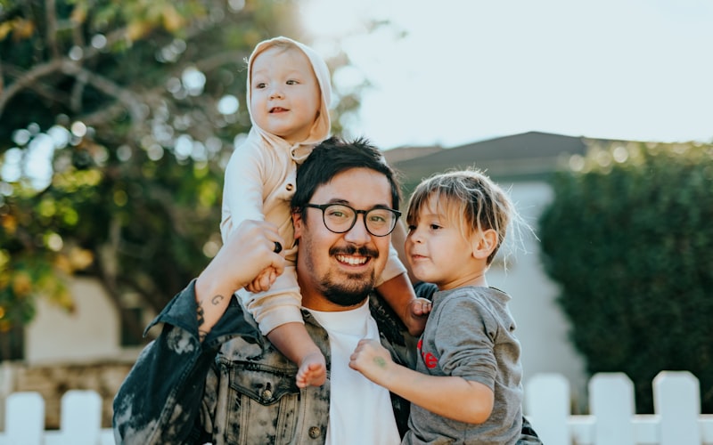 A father outdoors with his two young children, all smiling