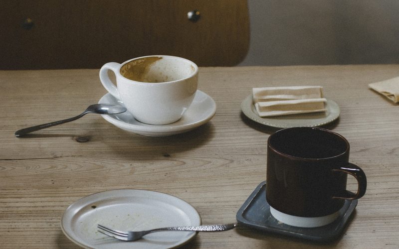Two empty cups and a cleared plate on a wooden table beside an empty chair