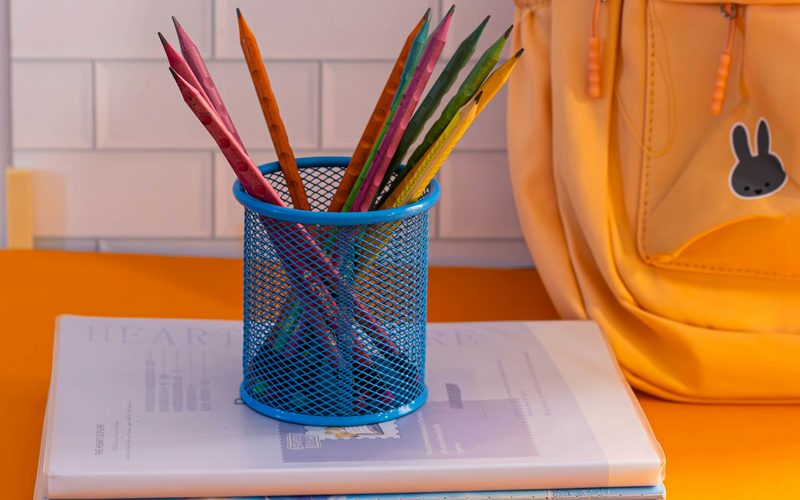 Coloured pencils, school books and a yellow school backpack on a table
