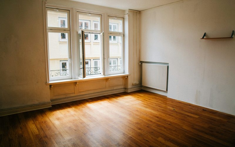 An empty room with a wooden floor and sunlight from a tall window