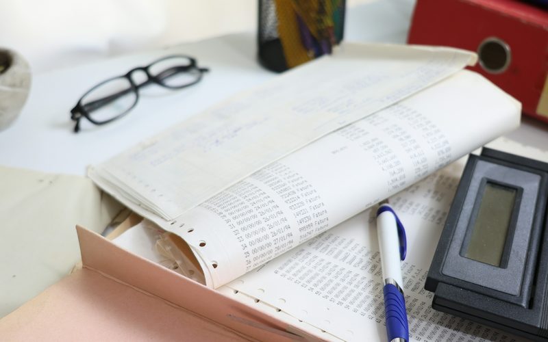 Printed accounts, reading glasses, a pen and a calculator on an office desk
