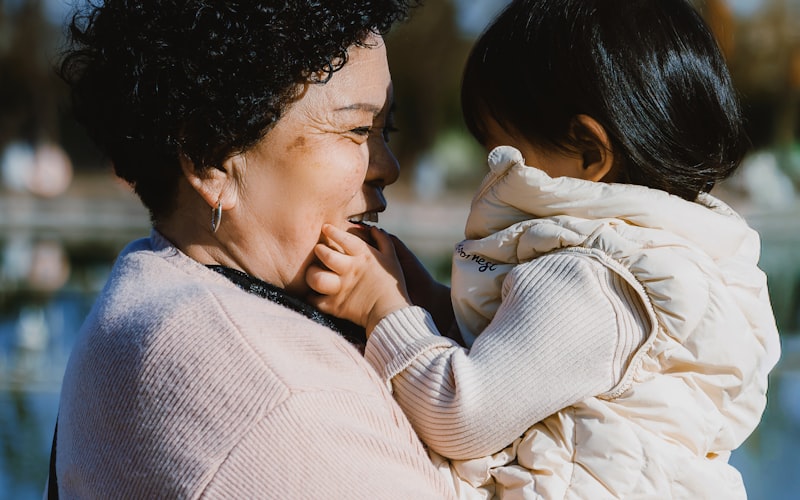 A grandmother laughing while holding her young grandchild outdoors